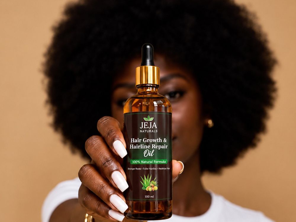 Woman with a full natural afro holding up a bottle of JEJA Naturals Hair Growth & Hairline Repair Oil