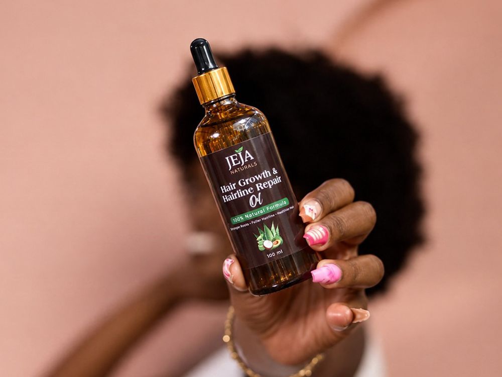 Hand holding a bottle of JEJA Naturals Hair Growth & Hairline Repair Oil in front of natural hair