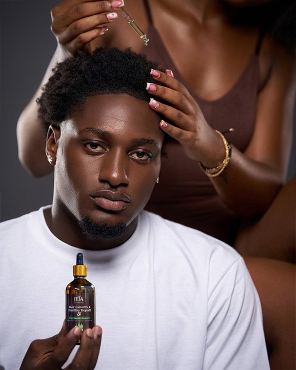 Man in a white t-shirt holding a bottle of JEJA Naturals Hair Growth & Hairline Repair Oil