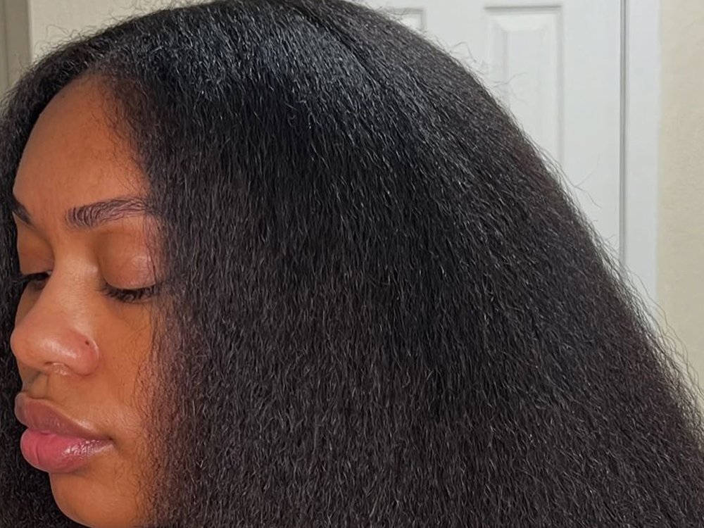 Person with silver-grey hair holding a bottle of JEJA Naturals oil, with more JEJA products in the background