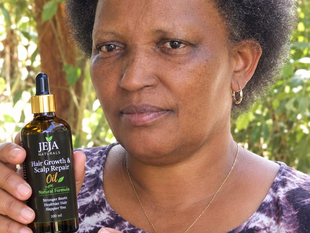 Woman holding a bottle of JEJA Naturals hair oil outdoors in the sunshine